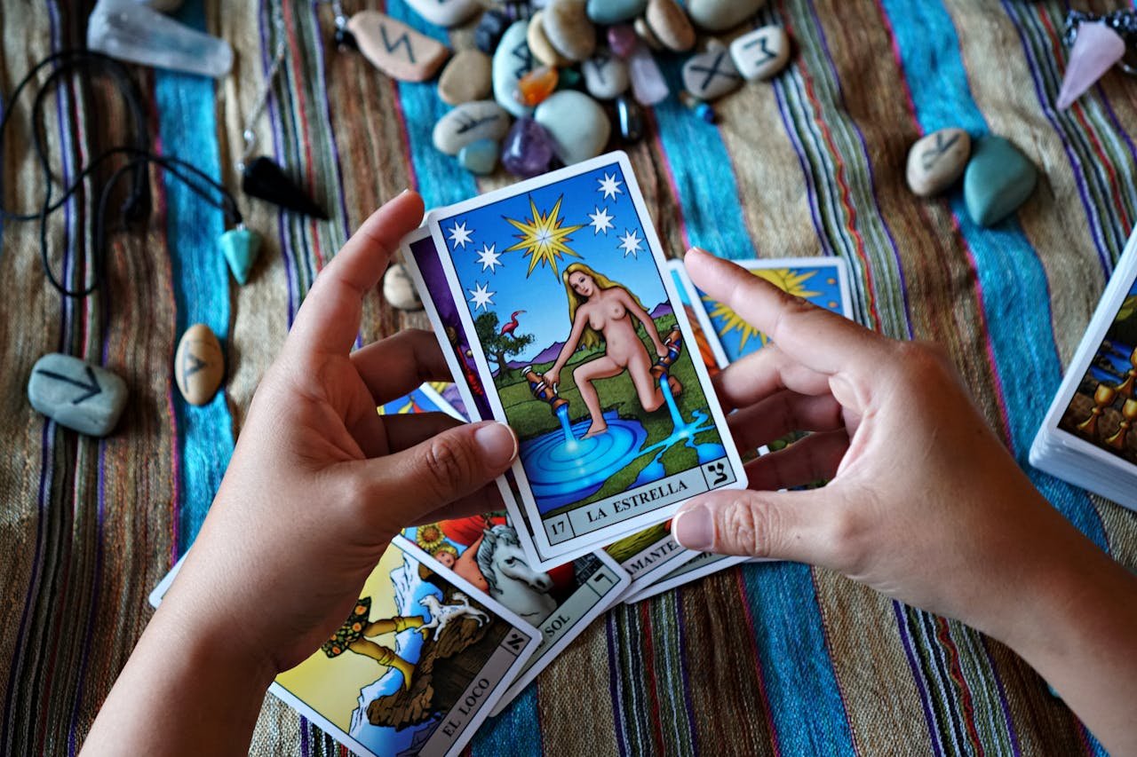 Hands holding a La Estrella tarot card, surrounded by stones and other cards.